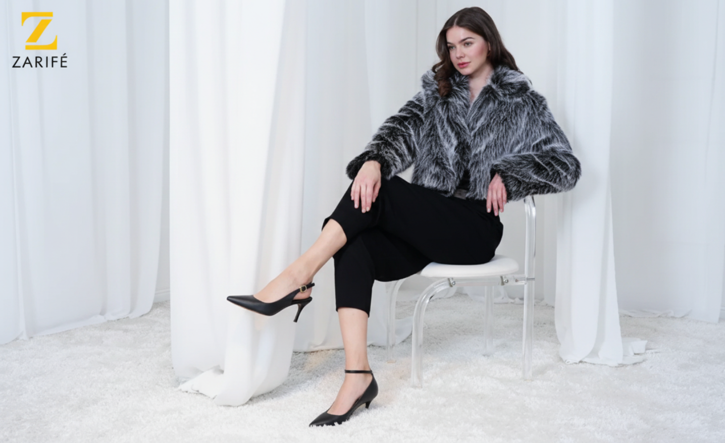 Woman wearing a fur coat sitting on a chair with white curtains in the background, branded 'Zarifé'. branded bags heels footwear sandals branded